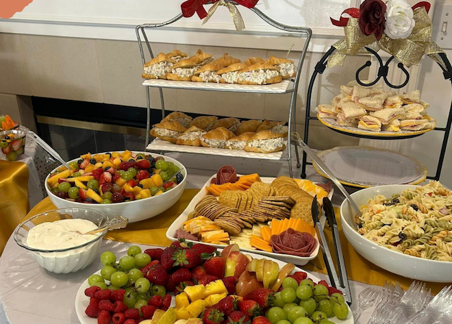 table set for party with sandwiches, cheese, crackers, fruit salad, pasta salad, and fresh fruit