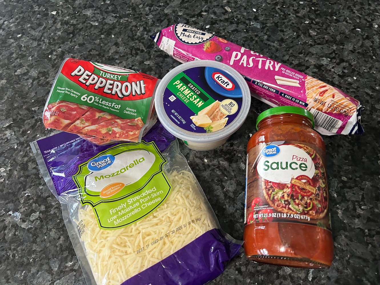 puff pastry pizza pinwheel ingredients laid out: pepperoni, parmesan, mozzarella, pizza sauce, puff pastry