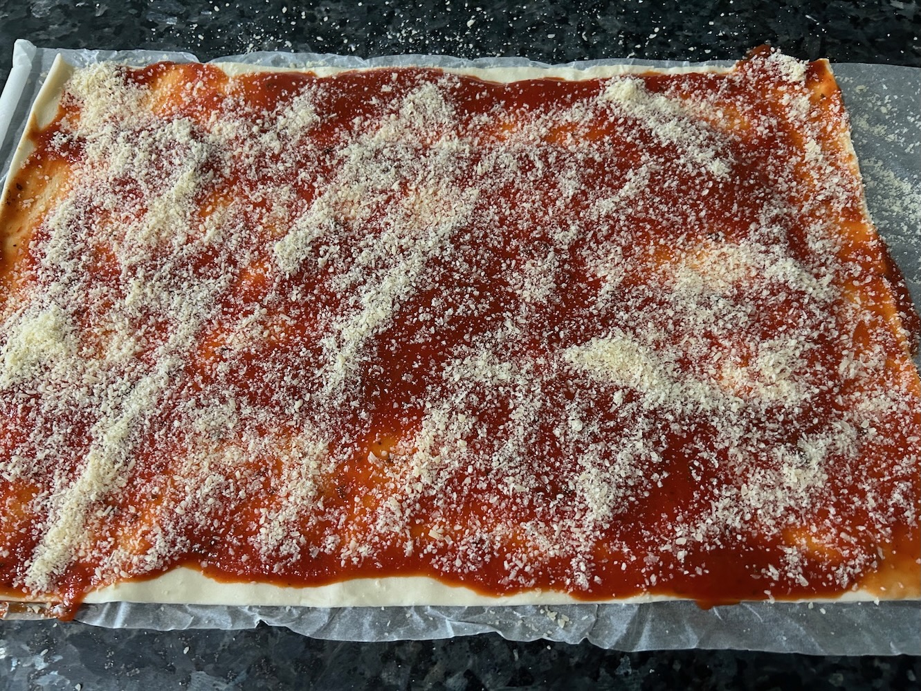 parmesan cheese on top of pizza sauce on puff pastry