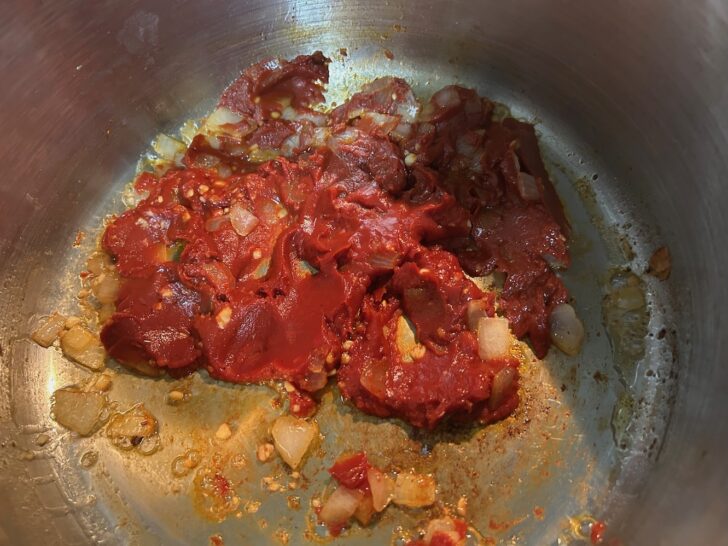 tomato paste in pan with onions, garlic, and butter