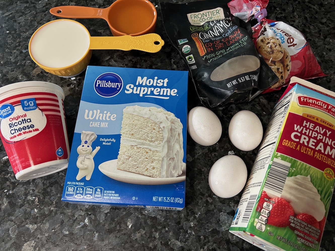 ingredients for cannoli cupcakes: white cake mis, ricotta, eggs, milk, oil, cinnamon, chocolate chips. Also frosting ingredients: whipping cream, ricotta (powdered sugar not in picture)