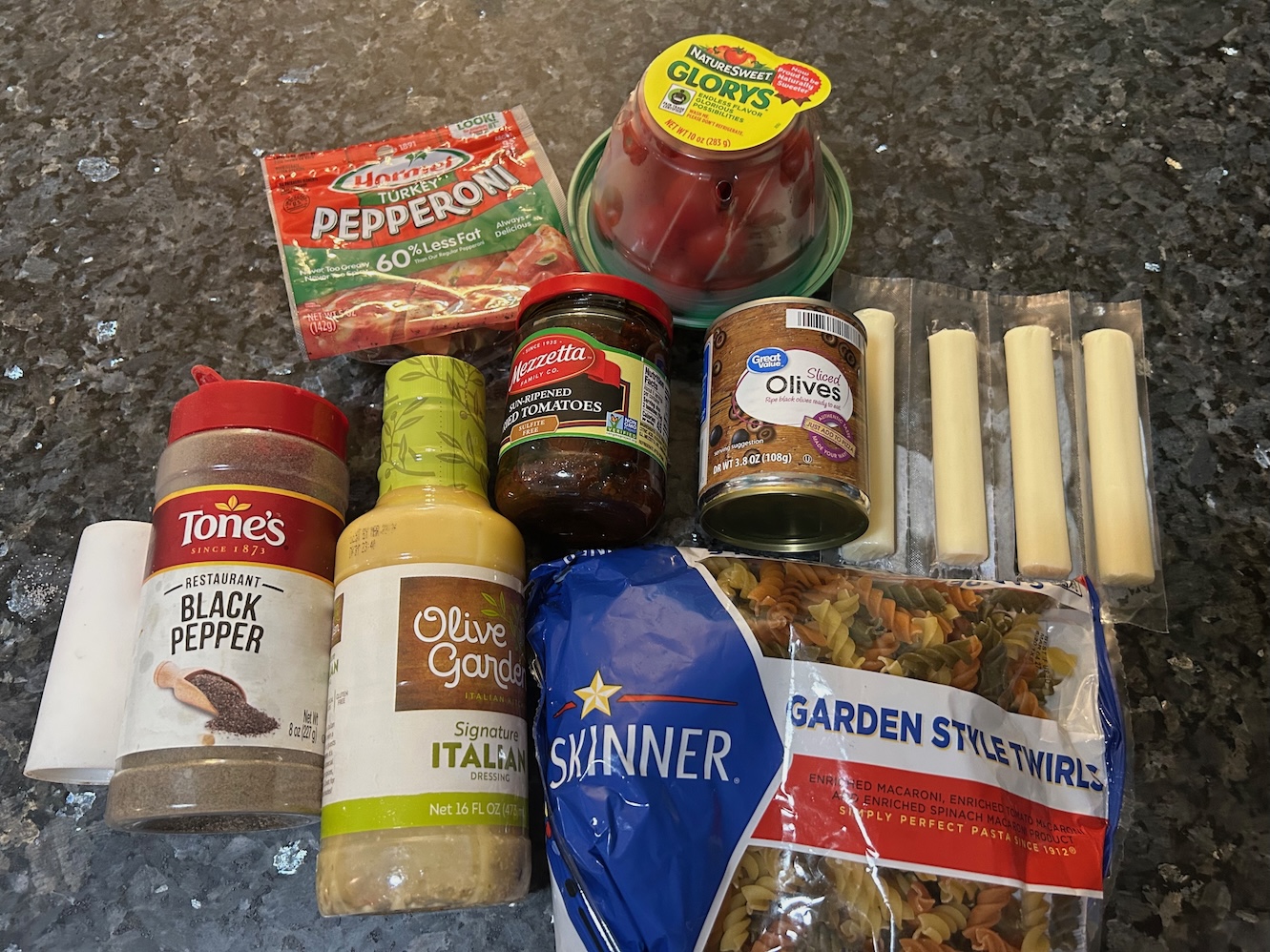 pasta salad ingredients: pasta, dressing, olives, sun dried tomatoes, cherry tomatoes, cheese, seasonings, pepperoni