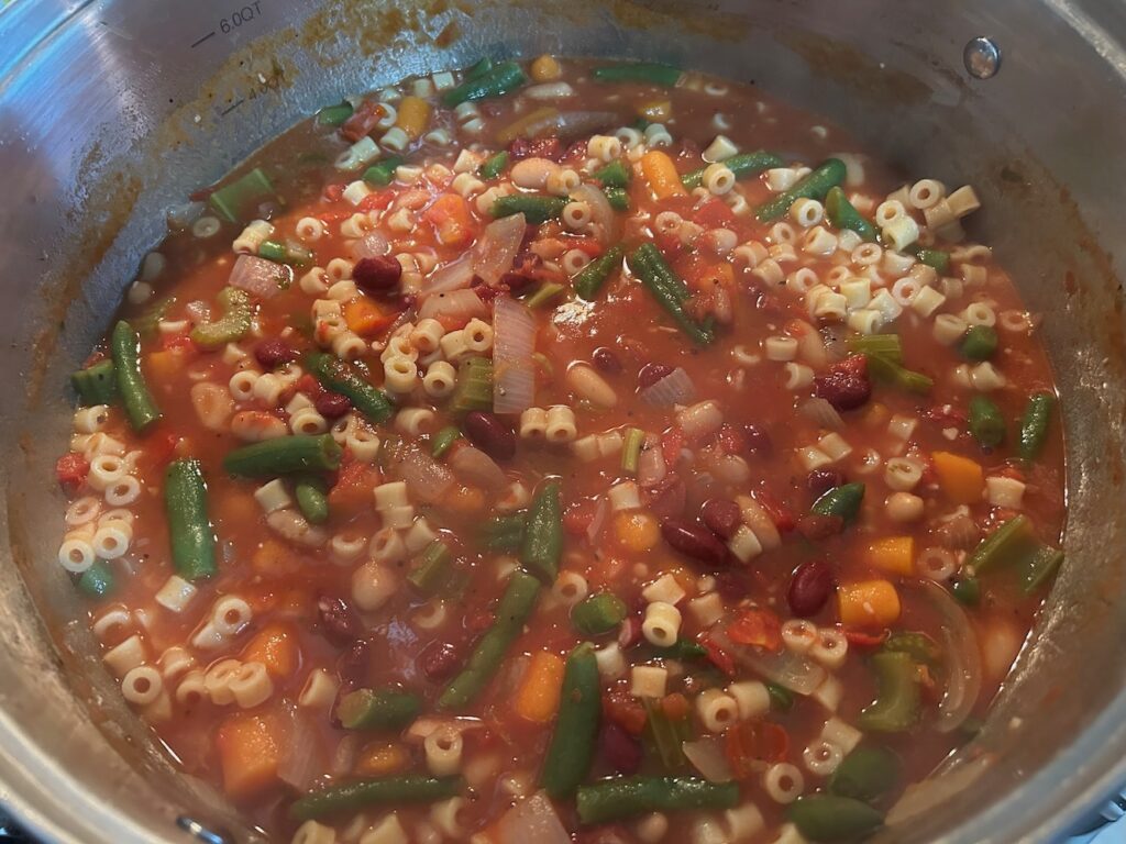 minestrone soup simmering in pot on stove, pasta added