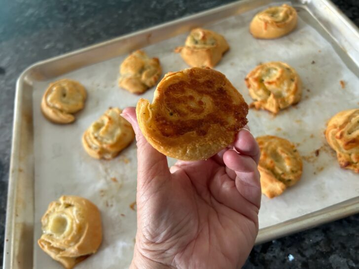 crescent roll pinwheels on baking sheet, one flipped over, revealing crispy bottom